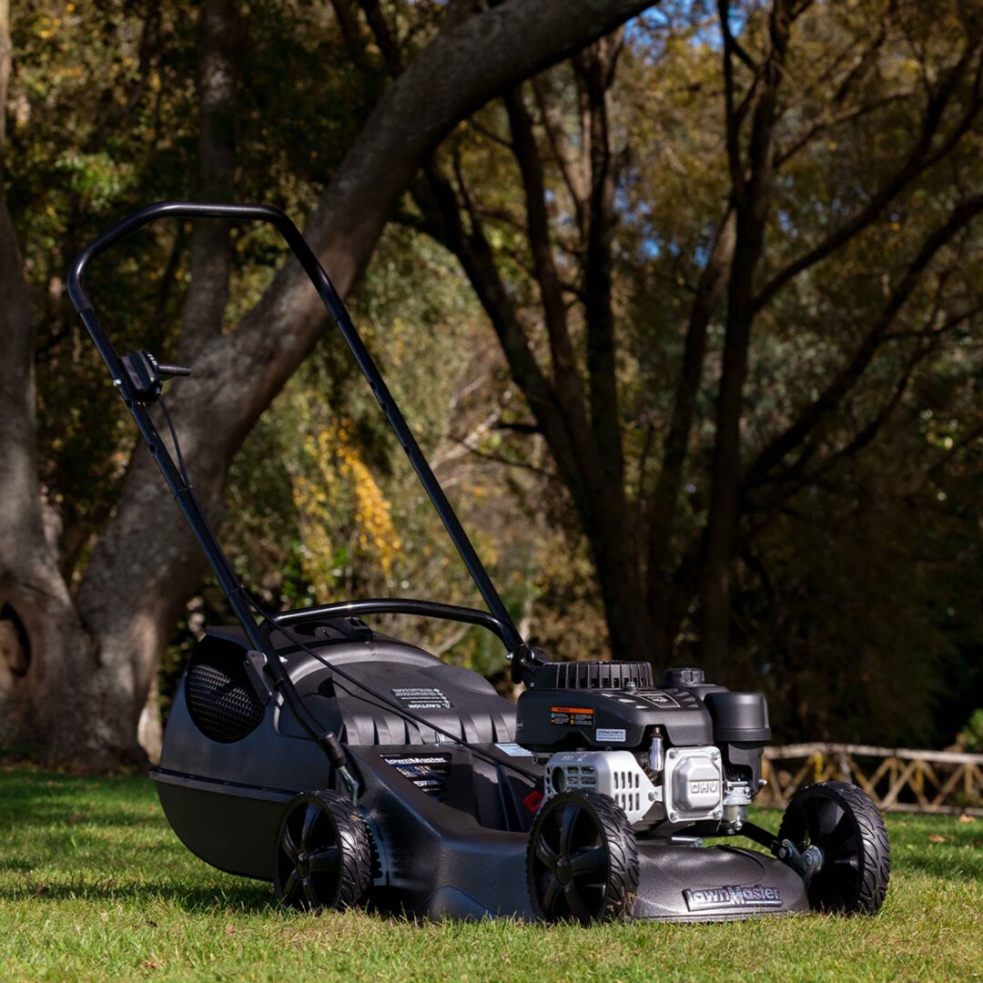 A black and gray lawnmower with a black handle and four wheels, positioned on a green lawn with a blurred background of trees.