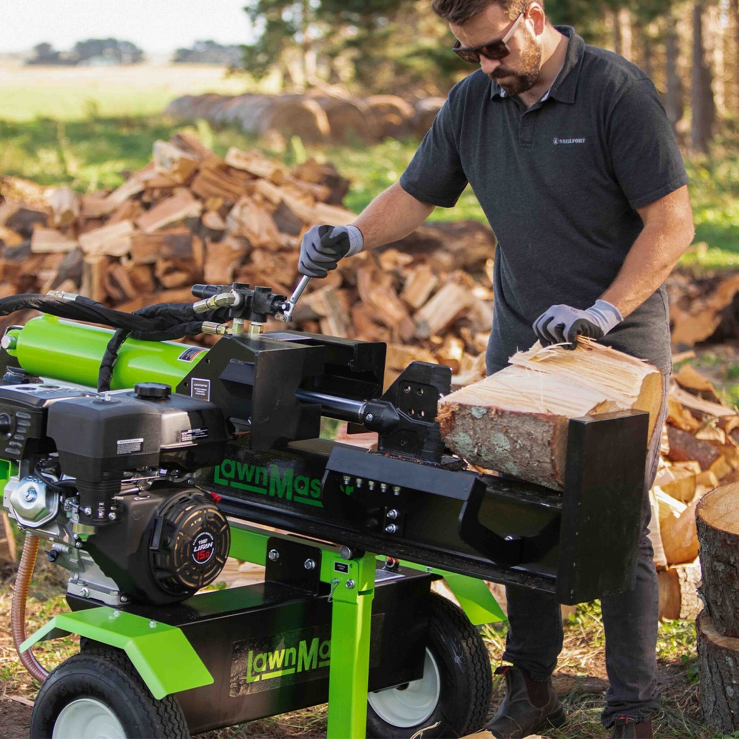 Man operating a green log splitter with wood in an outdoor setting