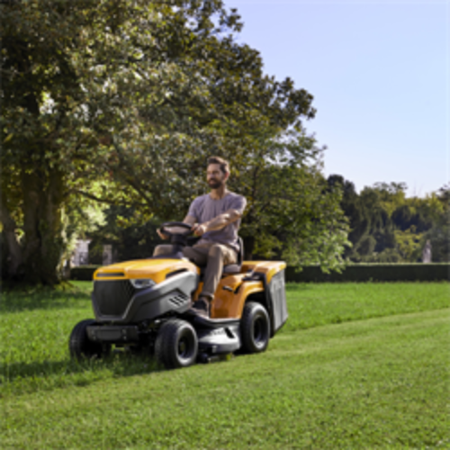Man operating a yellow Stiga Estate 598W riding lawn mower in a grassy area with trees in the background