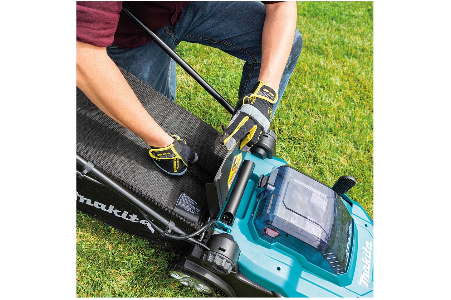 Man kneeling next to Makita lawnmower and lifting mower flap to remove catcher bag.