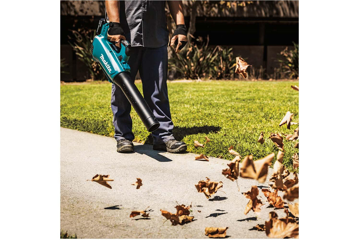 A Makita DUB184 blower in use outdoors blowing leaves