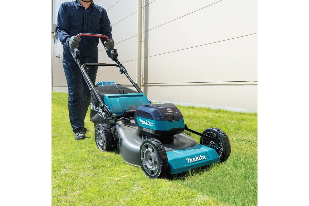 Person using a Makita lawn mower on grass with a white wall background